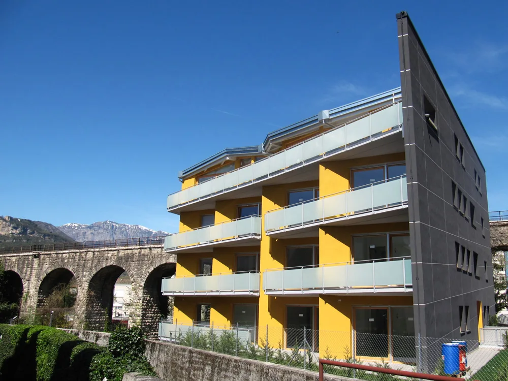 Casa gialla e nera a Trento, palazzina con balconi lunghi accanto a un viadotto ad archi